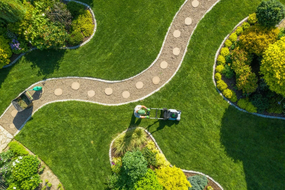 Gardener mowing a landscaped lawn from above